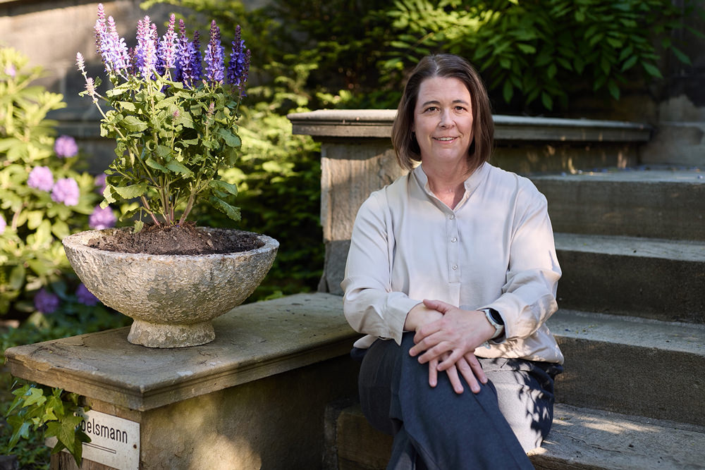 Valerie Wittmann im Garten Valerie Wittmann sitzt im Garten des DLMC-Standorts neben einer bepflanzten Steinschale.
